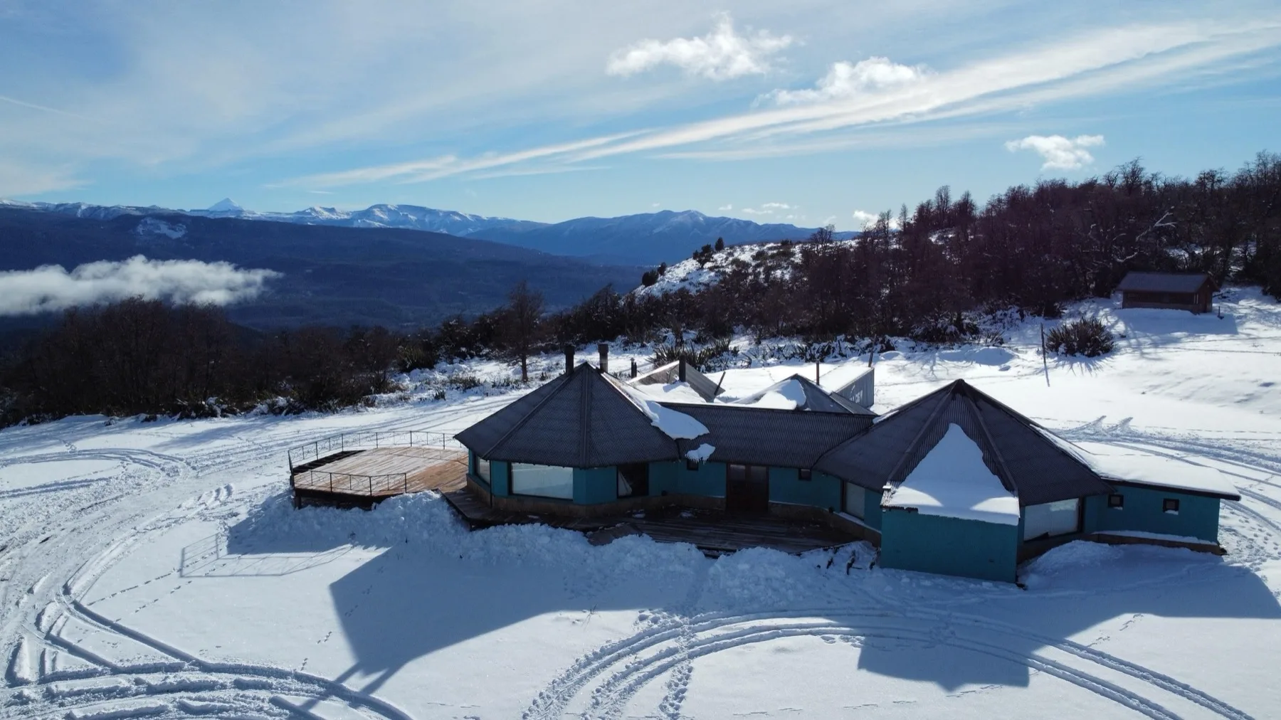 Vista aérea del refugio nevado en la montaña, con la cordillera y el Lanín de fondo